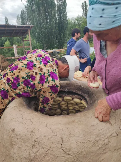 Un hombre se asoma a un gran horno tandoor de barro para colocar masa de pan en sus paredes, mientras es observado por una mujer y un grupo de viaje de WeRoad.