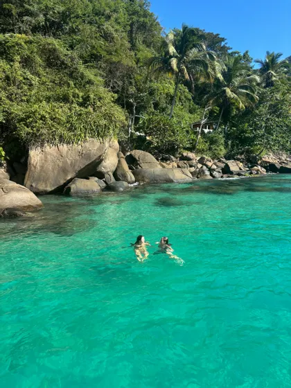 Deux personnes d'un voyage de groupe WeRoad nageant dans des eaux turquoise claires près d'une côte rocheuse couverte d'arbres verdoyants luxuriants.