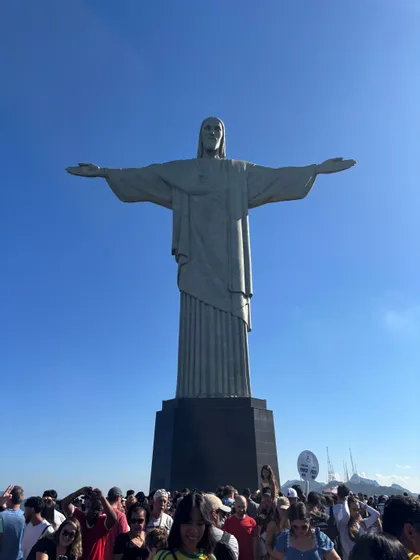 La statue du Christ Rédempteur domine une foule de gens à sa base, sous un ciel bleu clair.