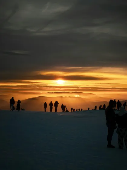 Sagome di un viaggio di gruppo WeRoad su una cresta di montagna innevata che osservano un'alba dorata su vette lontane.