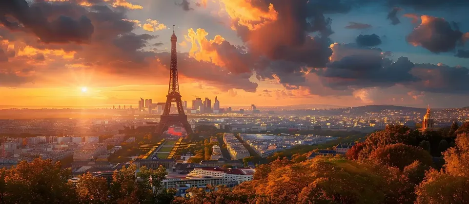 Un vasto paesaggio urbano con un'imponente torre a traliccio è illuminato da un tramonto arancione, con il fogliame autunnale in primo piano.