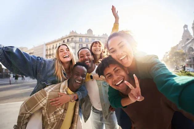 Un viaggio di gruppo WeRoad di amici che ridono e sorridono mentre si scattano un selfie su una strada di città soleggiata.