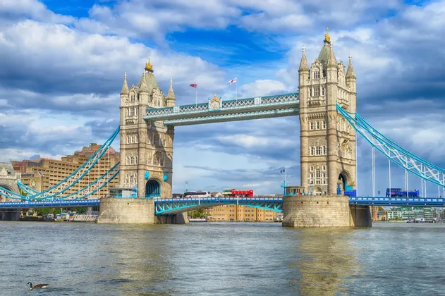 L'iconico Tower Bridge con le sue due torri che attraversano il Tamigi in una giornata luminosa e nuvolosa, mentre gli autobus rossi passano.