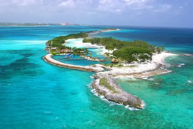 Una vista aerea di una piccola isola tropicale con spiagge di sabbia bianca, vegetazione lussureggiante e una piccola laguna, circondata da acqua turchese.