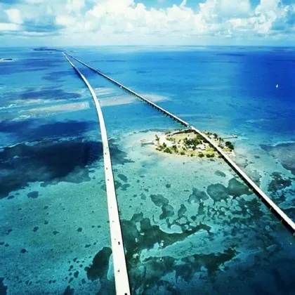 Una vista aerea di due lunghi ponti che si estendono su acque oceaniche turchesi, collegandosi a una piccola isola verde.