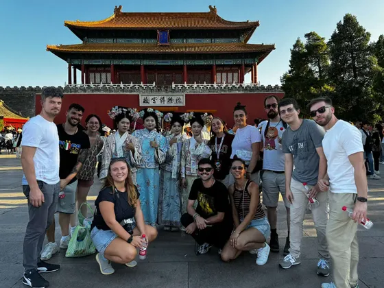 Un groupe WeRoad posant pour une photo avec des femmes locales en costumes traditionnels devant une porte historique rouge.