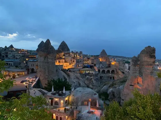 Un pueblo construido en formaciones rocosas distintivas, iluminado por luces cálidas bajo un cielo azul al atardecer.