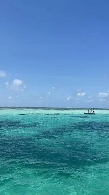 Un viaggio di gruppo WeRoad su una piccola barca che galleggia su un vasto oceano turchese, sotto un cielo azzurro limpido con nuvole leggere.