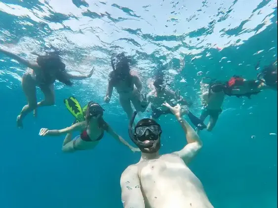 An underwater selfie of a WeRoad group trip snorkeling together in clear blue water, with bubbles rising to the surface.
