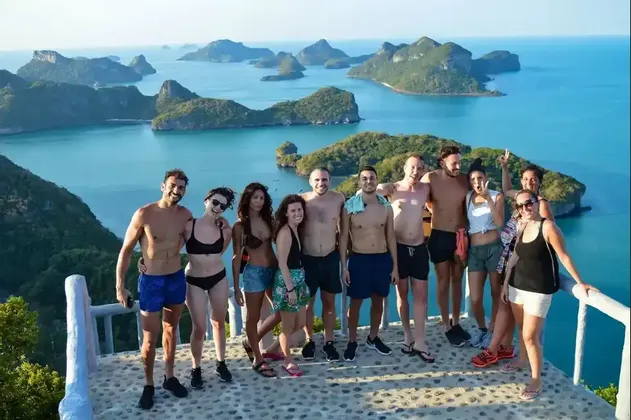 A WeRoad group trip smiles for a photo on a scenic viewpoint overlooking a bay with many green islands.