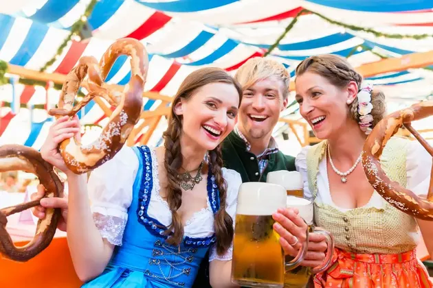 A WeRoad group trip of people in traditional outfits laughing together while holding large beers and pretzels.