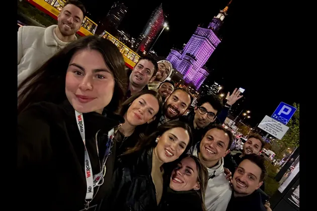 Un viaje en grupo de WeRoad sonríe para una selfie de noche en una ciudad, con un gran edificio iluminado de púrpura al fondo.