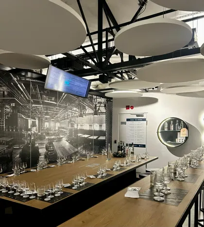 Largas mesas de madera con numerosas copas vacías en una moderna sala de catas con un mural industrial en blanco y negro en la pared.