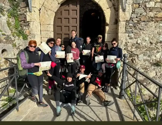 Eine WeRoad Gruppenreise posiert mit Zertifikaten auf einer Steinrampe vor einer gewölbten Holztür eines historischen Gebäudes.