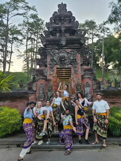 Un voyage de groupe WeRoad: des personnes en sarongs colorés posent pour une photo sur les marches d'un temple de pierre orné.
