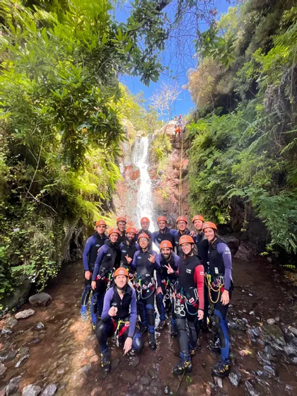 Un viaggio di gruppo WeRoad con mute e caschi posa per una foto in un ruscello alla base di una cascata durante un'attività di canyoning.
