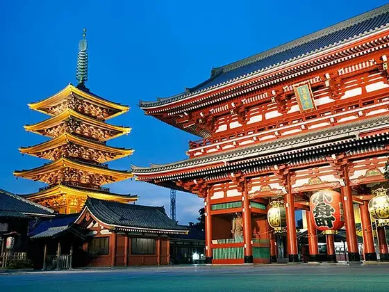 Una tradizionale pagoda giapponese e un grande cancello rosso di un tempio sono illuminati al crepuscolo sotto un cielo blu profondo.