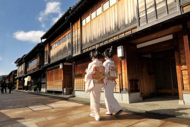 Due donne in kimono tradizionali camminano lungo una strada lastricata fiancheggiata da storici edifici giapponesi in legno.