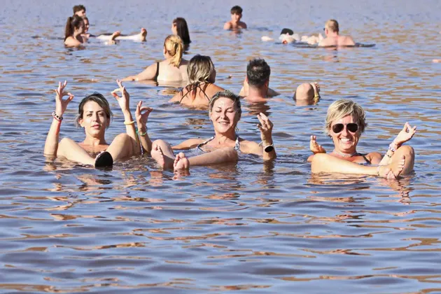 Un viaje en grupo de WeRoad flotando y relajándose en un lago, con tres mujeres en primer plano sonriendo y haciendo gestos.