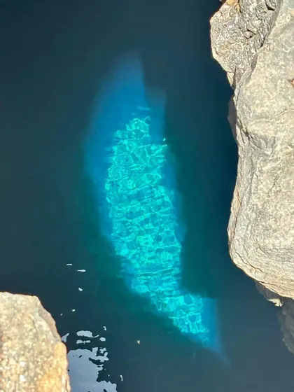 Un parche de agua turquesa vibrante es iluminado por la luz del sol dentro de una piscina natural oscura y rocosa.