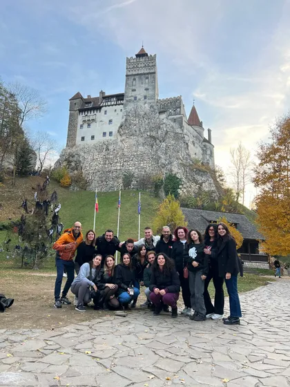Un viaggio di gruppo WeRoad di persone in posa per una foto su un sentiero di pietra davanti a un grande castello appollaiato su una collina rocciosa.