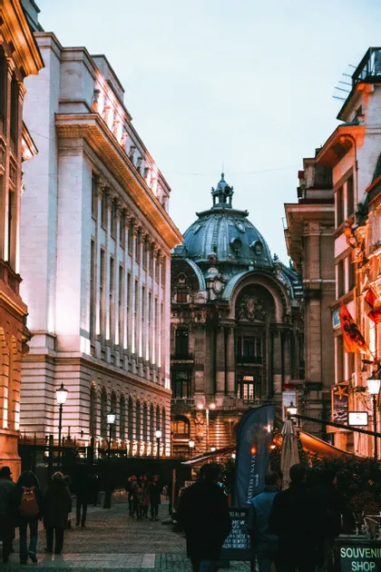 Un edificio decorato con una grande cupola si erge alla fine di una strada di ciottoli dove le persone camminano al tramonto.