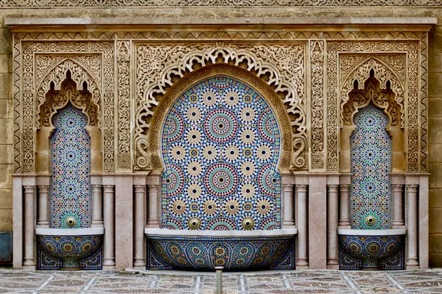 Una sontuosa fontana pubblica, adornata con colorate piastrelle a mosaico geometriche e incorniciata da archi in pietra scolpiti.