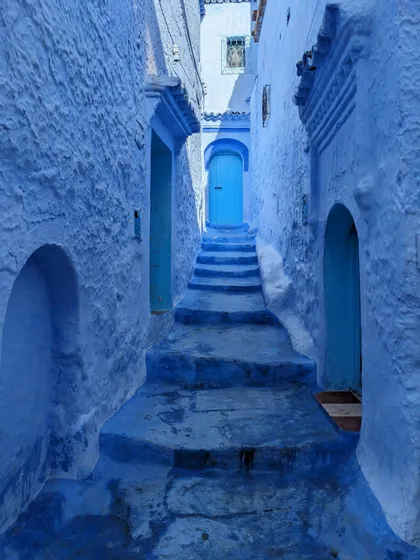 Una tortuosa scalinata in pietra sale attraverso uno stretto vicolo, con pareti, gradini e una porta ad arco, tutti dipinti di blu.