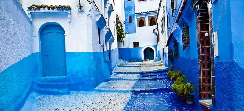 Un vicolo stretto e tortuoso in ciottoli, con scalini in pietra tra edifici dipinti in vivaci tonalità di blu e bianco.
