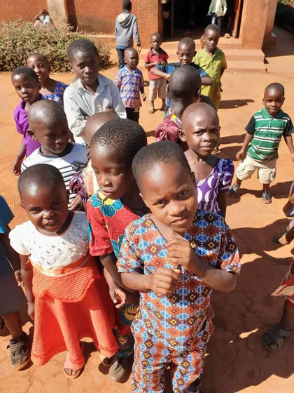 Ripresa dall'alto di un gruppo di bambini con vestiti colorati in piedi su un terreno di terra rossastra.