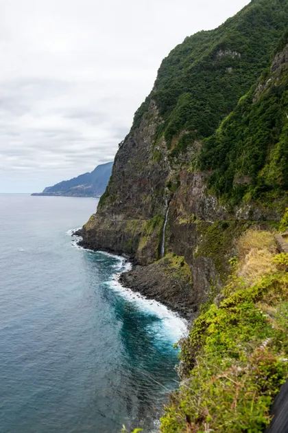 Una cascata si getta giù da una ripida scogliera verdeggiante nell'oceano, con le onde che si infrangono contro la costa rocciosa sottostante.