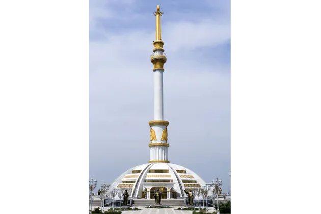 Un alto monumento bianco, con guglia e dettagli dorati, si erge su una base a cupola in un'ampia piazza sotto un cielo nuvoloso.