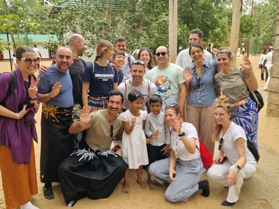 Eine WeRoad-Gruppe posiert für ein Foto mit zwei einheimischen Kindern, lächelnd und winkend im Freien.