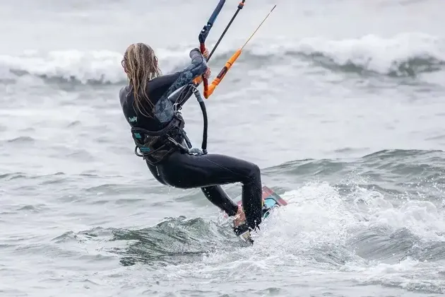 Una persona in muta nera, vista da dietro, che fa kitesurf su acqua mossa con onde.