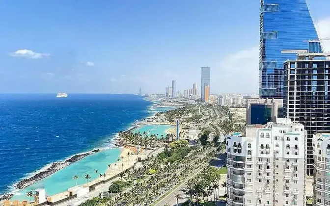 Una vista aerea del litorale di una città moderna con grattacieli, palme e spiagge con acqua turchese accanto a un mare blu profondo.
