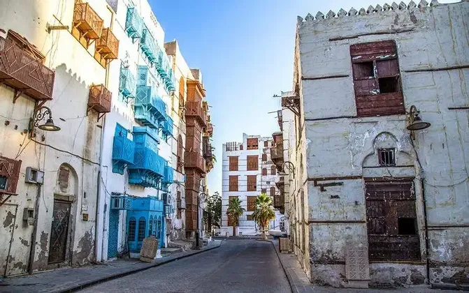 Una strada stretta e vuota affiancata da edifici storici con muri imbiancati a calce e balconi in legno intagliati blu e marroni.