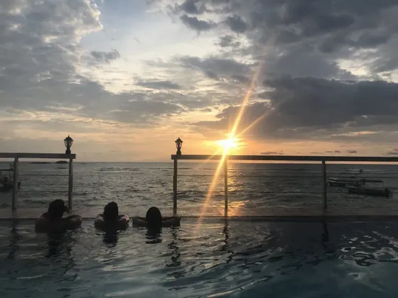 Un viaggio di gruppo WeRoad con tre persone che si rilassano in una piscina a sfioro ammirando il tramonto sull'oceano.