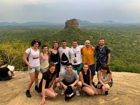 Eine WeRoad-Gruppenreise posiert für ein Foto auf einem felsigen Aussichtspunkt mit Blick auf ein üppiges Tal und eine ferne Felsenfestung.