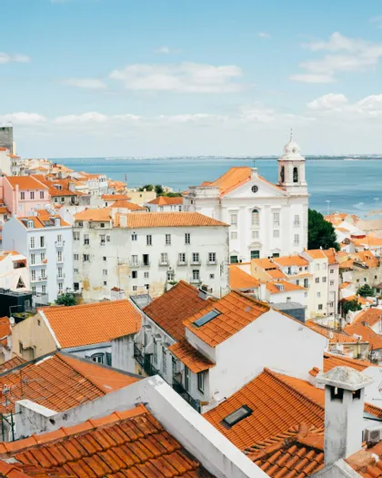 Una vista dall'alto di una città con tetti in tegole arancioni e edifici bianchi che si affacciano su un grande specchio d'acqua sotto un cielo azzurro.