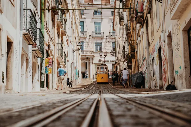 Une vue en contre-plongée d'un tramway jaune montant une rue raide et étroite sur des voies pavées, bordée de hauts bâtiments et de piétons.