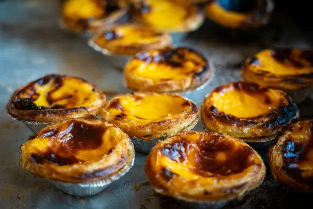 Gros plan sur plusieurs pastéis de nata fraîchement cuits, les célèbres tartelettes portugaises à la crème, sur une plaque de cuisson en métal.