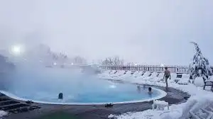 Quelques personnes se détendent dans une piscine extérieure fumante entourée d'un paysage entièrement enneigé.