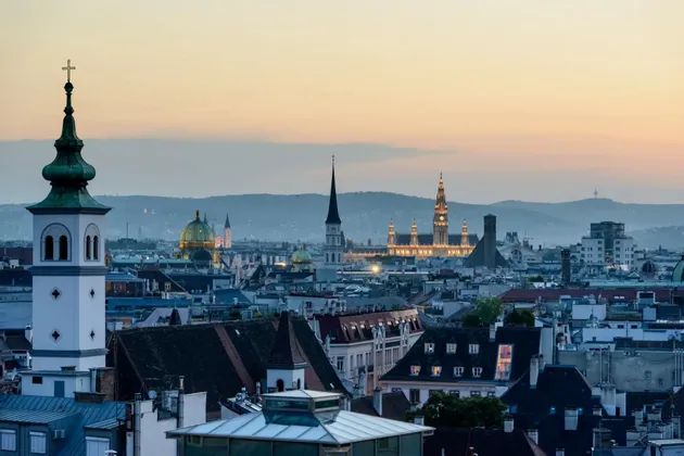 Skyline storico di una città con numerose guglie e cupole di chiese, visto dall'alto al tramonto e con colline sullo sfondo.
