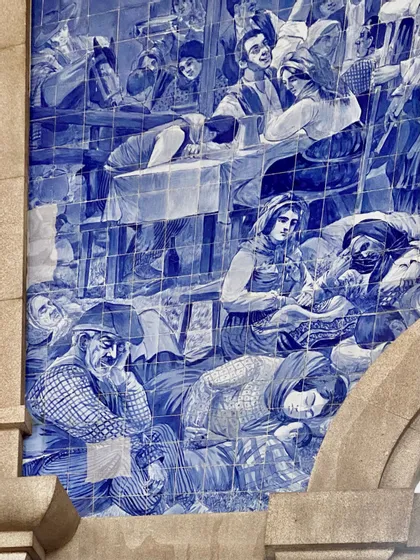 Primer plano de un mural de azulejos azules y blancos que representa una escena histórica con personas descansando e interactuando.