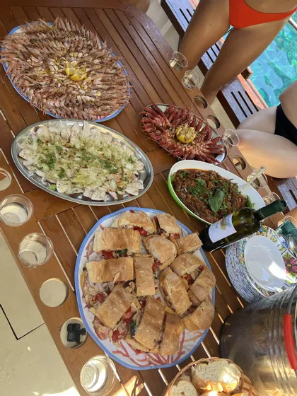 Un gruppo WeRoad in viaggio cena in barca, con una tavola imbandita di frutti di mare freschi, panini e vino bianco.