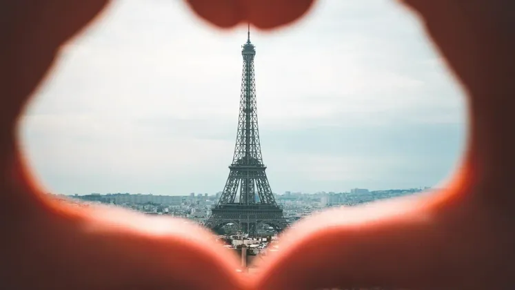 La Torre Eiffel incorniciata da un cuore formato dalle mani, con lo skyline della città sullo sfondo.