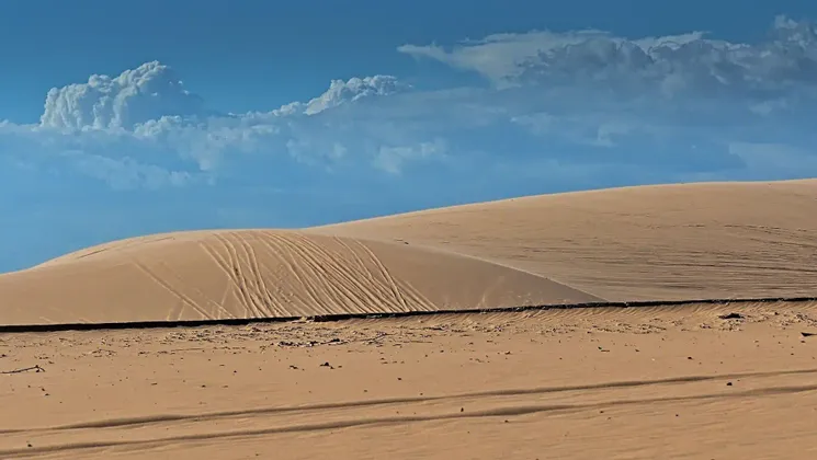 Vaste dune di sabbia dorata con tracce sui loro pendii sotto un cielo azzurro parzialmente nuvoloso.
