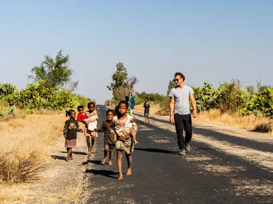 Un uomo di un viaggio di gruppo WeRoad cammina con un gruppo di bambini locali su una strada asfaltata in un paesaggio rurale e arido.
