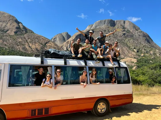 Un gruppo WeRoad in posa per una foto sul tetto e dai finestrini di un minibus, davanti a una catena montuosa rocciosa.