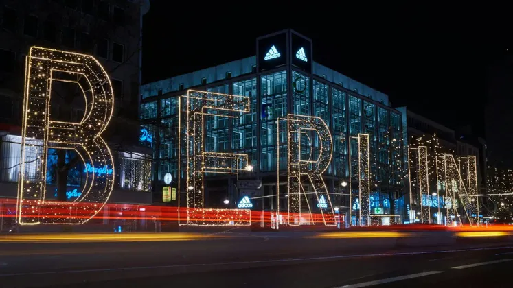 Un grande cartello illuminato che forma la scritta BERLINO su una strada cittadina di notte, con scie luminose a lunga esposizione lasciate dalle auto che passano.